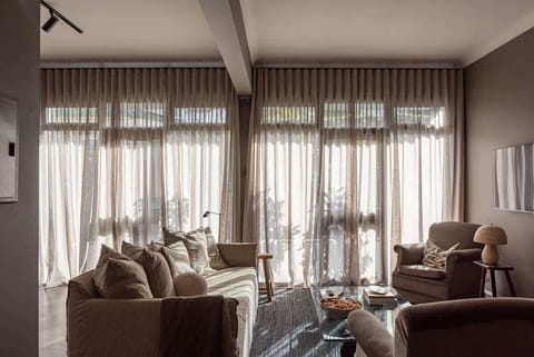 Vintage armchairs covered in soft velvet, a comfortable linen sofa and sunlight curtains form a warm, inviting space.