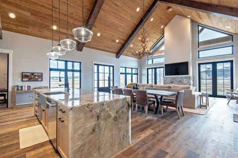 Vaulted great room with hand-hewn beam ceiling, antler chandelier, and a 270° view of the Teton range — the kind of space guests photograph the moment they walk in.