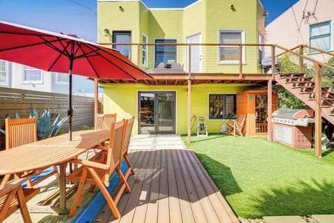 Soak up the sunshine on the spacious wooden deck, where a vibrant red umbrella shades the outdoor dining table and the bright, cheerful home opens up to a private grassy backyard perfect for relaxing afternoons