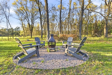 Outdoor firepit area with Adirondack seating, stacked firewood, and a peaceful wooded backdrop for relaxing evenings.