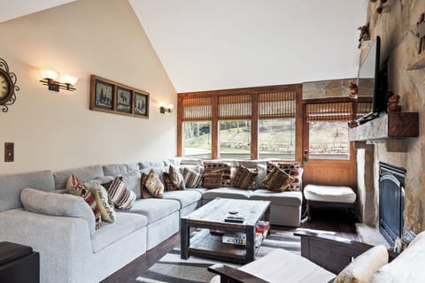 - Living room with soft sectional sofa and inviting mountain décor  
- Stone fireplace with mounted TV makes evenings cozy and warm  
- Board games and rustic touches enhance cabin-style charm