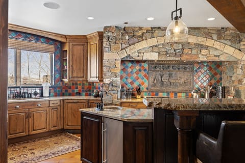 A view of a chefs kitchen with with large stove and tile backsplash and view from window of the mountains