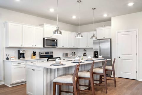 Sleek white kitchen with island seating, stainless appliances, and pendant lighting.
