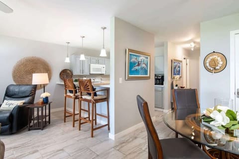 Open concept with pendant lights, bar stools, and a view from kitchen to dining and entry hallway.

