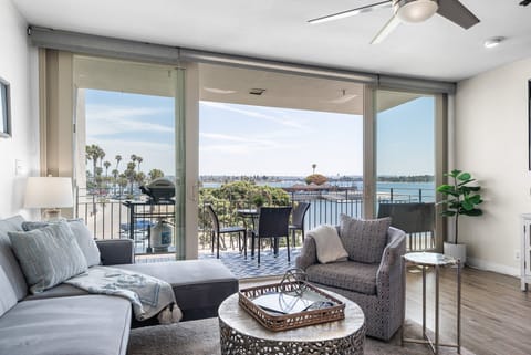 Bright and airy living room featuring comfortable seating, a large TV, and sliding glass doors that open to a private balcony with stunning views of Mission Bay, perfect for relaxing with a morning coffee or enjoying the sunset.