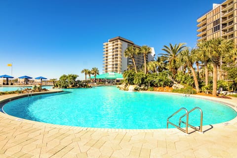 Relax by the large outdoor pool surrounded by tropical landscaping and resort buildings.
