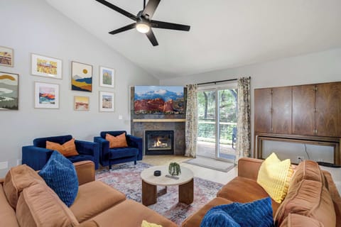 Gather in the bright living room where two cozy sofas face a stone fireplace and coffee table, with colorful wall art and a large window bringing in natural light—an inviting spot to chat, read, or unwind together after a day out.