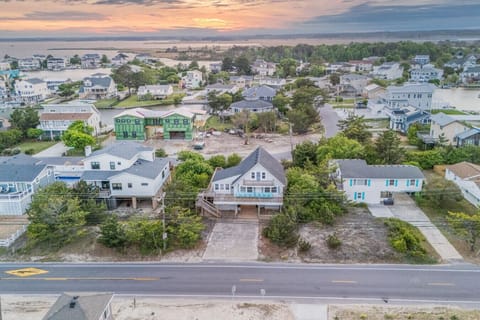 Aerial sunset view of a quiet coastal neighborhood with beach homes, tree-lined streets, and nearby water. Elevated houses and sandy lots create a relaxed seaside feel, just moments from the shore and local attractions.