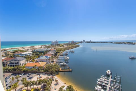 Aerial view of the property's waterfront location on a calm bay, with sandy beaches, boat docks, and coastal homes stretching along the shoreline beneath clear blue skies.