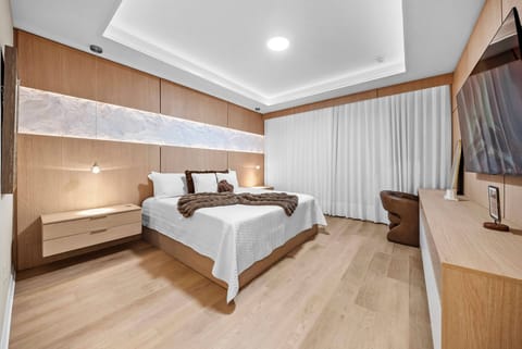 This beautifully designed bedroom, with warm wood accents and soft neutral tones, creates a calming atmosphere. Generous natural light filters through sheer curtains, illuminating the plush bedding for your restful nights.