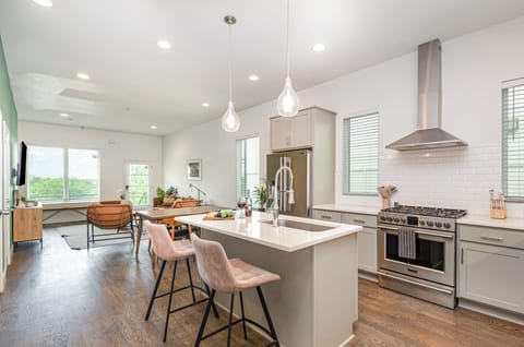 Unit 1: Bright open-concept kitchen featuring a quartz-topped island with bar seating, stainless steel appliances, and abundant natural light streaming through the windows.