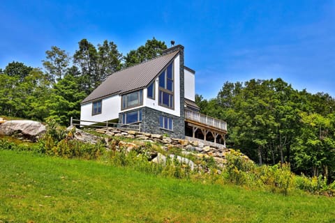 3-story Vermont chalet on sloping terrain, with lawn and trees all around beneath a clear blue sky.