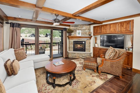 Cozy living area featuring a plush sectional sofa, stone fireplace with mounted TV, and expansive windows that open to a private patio.