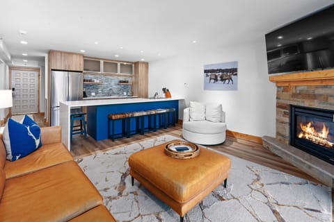 Inviting open-concept living space featuring a modern kitchen flowing seamlessly into a cozy living area with a sectional sofa, stone fireplace, and large windows that open to a private balcony.