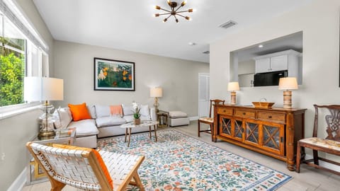 Step into a sunlit, artful living space with tropical flair—featuring bold pops of orange, vintage wood accents, and a large smart TV for cozy nights in. The perfect blend of El Cid charm and West Palm warmth