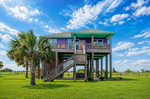 Elevated beach house exterior at Anderson Avenue, Bolivar Peninsula, TX, featuring raised coastal construction, spacious grassy yard, and exterior staircase access.
