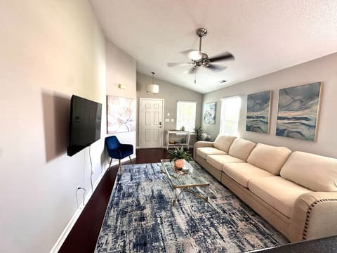 Bright, open living room with large TV, cream sofas, and coastal wall art — your space to unwind