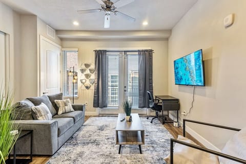 Bright living area w/ cozy sofa, wall-mounted TV & tall windows bringing in natural light