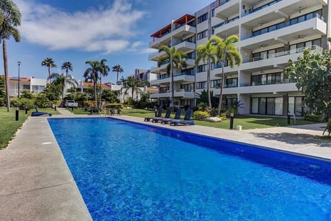 Shared sparkling resort-style pool stretching alongside the building, framed by palms & lounge areas for sunny days outdoors
