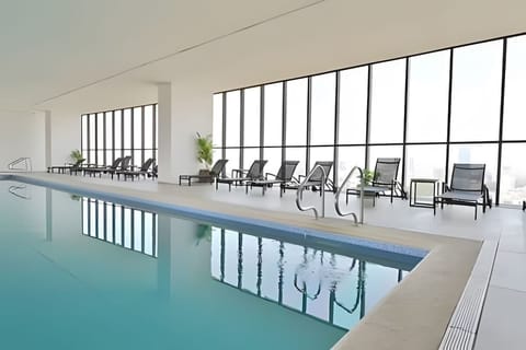 Shared indoor pool lined w/ loungers & floor-to-ceiling windows for a refreshing swim in natural light