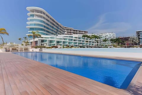 Resort-style shared pool stretching along the modern beachfront building under clear blue skies