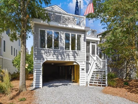 The modern design of this vacation home includes large windows capturing natural light, complemented by a relaxing outdoor area and convenient parking beneath a raised structure.