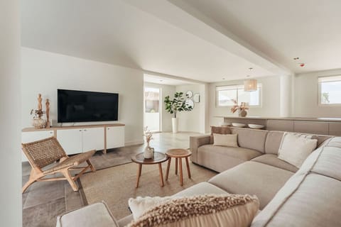 A cozy living room with a beige sofa, TV, wooden chair, and natural light for a relaxing vibe.