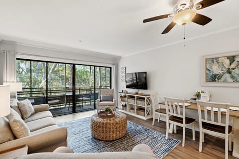 Bright living room with a smart TV, opening onto a screened-in balcony overlooking the trees.