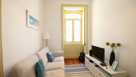 Relax in this charming and sunlit living room featuring classic Portuguese shutters, a plush beige sofa, and tasteful beach-themed artwork — the perfect nook for unwinding after a day in the city. #FigueiraApartment #CozyLiving #ShortTermRental