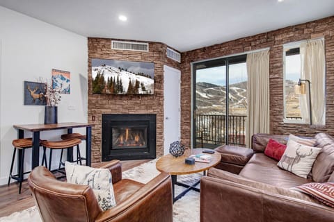 Cozy up by the fireplace with mountain views stretching beyond your windows, featuring rich leather seating and rustic stone accents.