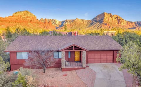 A charming home nestled among desert landscape with striking red rock formations in the background.