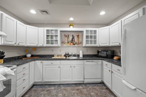 Fully stocked kitchen with white appliances, stainless sink, dishwasher, microwave, toaster, and coffee maker.