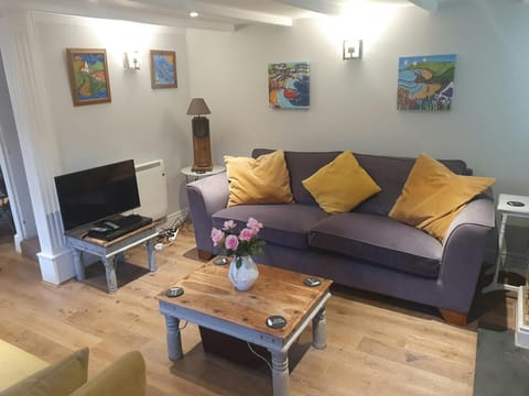 Sirring room with wooden floors. TV, coffee table grey sofa with yellow cushions