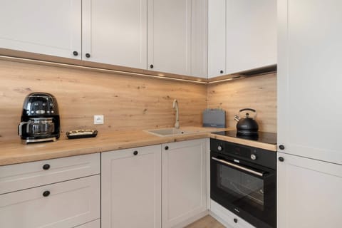 A compact kitchen with modern appliances, white cabinetry, and a wooden backsplash.