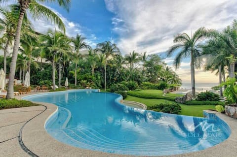 Shared pool framed by palm trees & lush gardens, a serene tropical spot to cool off under the sun.