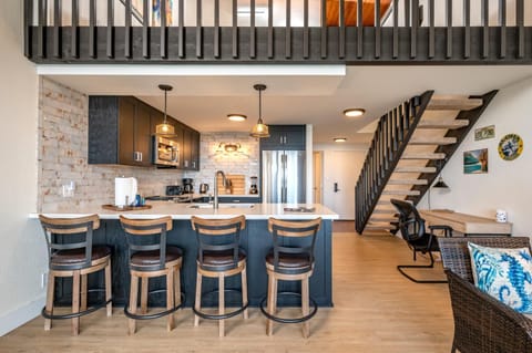 This modern kitchen features sleek dark cabinetry, pendant lighting, and a brick backsplash that adds rustic charm     NAP-C43
