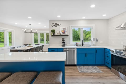 Your spacious gourmet kitchen invites culinary adventures with sleek blue cabinetry, gleaming countertops, and garden views through oversized windows.