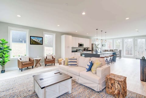 A cozy living room with two side chairs and a small table, complemented by a kitchen bathed in natural light from the glass window.
