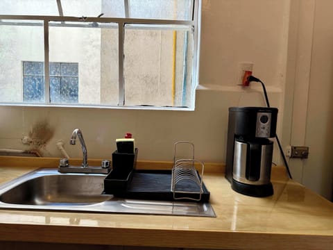 Cocina (tarja para lavar trastes, cafetera, mueble de madera, bote de basura blanco y escurridor de trastes negro)