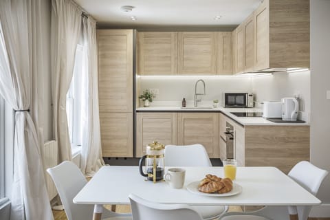 Highlights a light-wood, L-shaped kitchen with modern appliances, under-cabinet lighting, and a dining area with a white table and chairs.