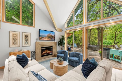 Wall of windows, fireplace glow, and forest all around.
