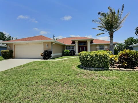 Single-story home featuring a two-car garage, manicured lawn, and tropical landscaping at the entry