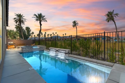 Private pool w/ cascading waterfalls glowing under a vibrant sunset sky