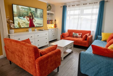 Seating area with orange sofas, a blue sofa with cushions, a white coffee table, and a wall-mounted TV.