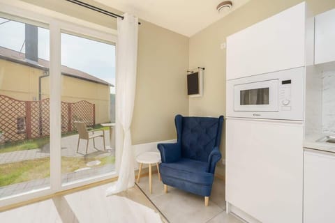  In the spacious bedroom, a comfortable navy armchair is positioned in the corner of the room. In the background, a glimpse of the kitchenette with white cabinets highlights the apartment's functionality.