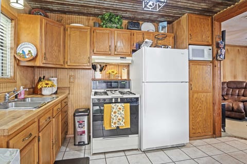 A fully equipped rustic kitchen featuring wooden cabinets, a white refrigerator, a stove, a microwave, and a cozy corrugated metal ceiling, offering all the essentials for a comfortable stay.