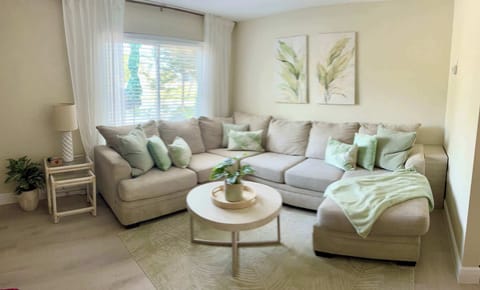 Bright living room with a large beige sectional sofa and soft green accents.