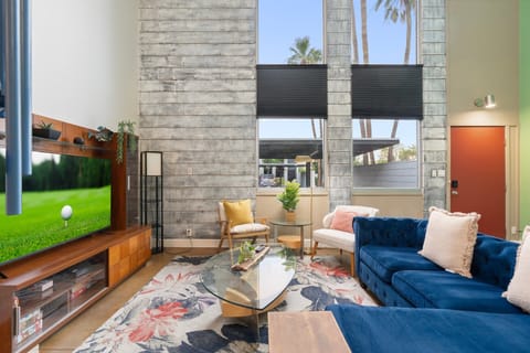 Tall ceilings and a wall of windows flood this living area with light, anchored by a large TV, layered rugs, and deep seating. It’s an easy spot to kick back after a day out, stretch your legs, and enjoy a relaxed evening indoors.