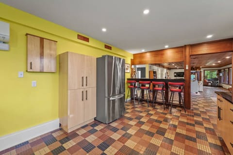 Kitchen view toward the open living area, highlighting the spacious layout, stainless steel refrigerator, and seamless flow between cooking and entertaining spaces.