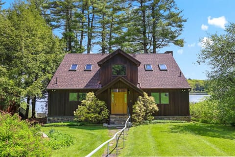 Charming lakefront cabin surrounded by tall pines, featuring a rustic wood façade and a welcoming front path.